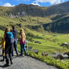 Familie genießt das Liechtenstein wandern in den Alpen. Grüne Hänge, kleine Häuser und ein majestätischer Berg im Hintergrund.