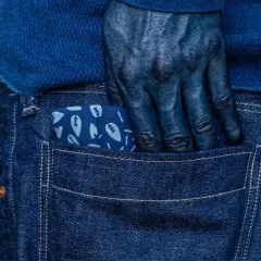 Main bleue, main plongée dans la poche d'un jean, le tissu orné de feuilles, témoignage de la teinture.