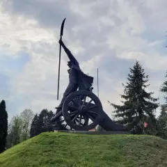 Pomnik Kościuszki z kosą na armacie, symbol zwycięstwa pod Racławicami, na tle pochmurnego nieba i drzew.