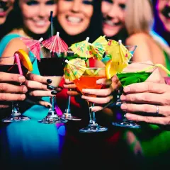 Amici brindano con cocktail colorati in un vivace night club a Monaco, tra risate e luci soffuse.