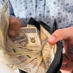 Ręce trzymają portfel z banknotami 200 zł. To może być symbol nagród jubileuszowych w PKP PLK, zasłużona gratyfikacja za lata pracy.