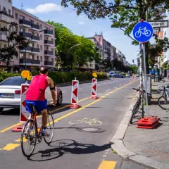 Ein Mann fährt auf einem pop-up Radweg in Berlin. Absperrungen markieren den Weg, der von Autos und Gebäuden gesäumt ist.