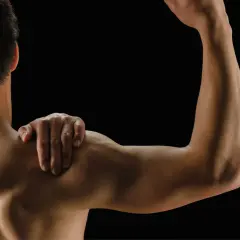 Mężczyzna z ręką na ramieniu, pokazujący umięśnione plecy i biceps. Białko po treningu wspiera regenerację mięśni.