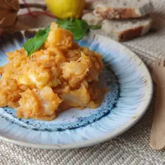 Un plato de col con patatas, guisado y servido con hojas verdes. Acompañado de pan y limón.
