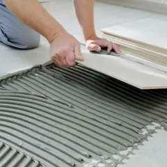 Hands carefully place a tile over cement board, with a stack of tiles nearby.