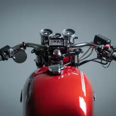 Manubrio di una moto custom rossa con specchietti, tachimetro e contagiri.