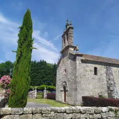 Iglesia de piedra bajo cielo azul, con un ciprés alto y flores rosas. Un lugar tranquilo en Cova da Moura.