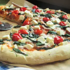 Pyszna pizza z fetą, pomidorkami koktajlowymi i szpinakiem, gotowa do pokrojenia.