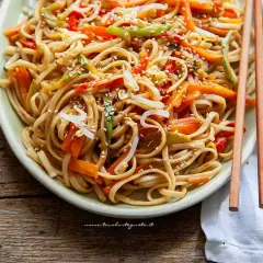 Noodles con verdure colorate, carote, peperoni e germogli di soia, guarniti con semi di sesamo.