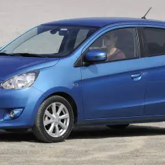 Niebieski Mitsubishi Mirage, idealny dla szukających bezawaryjnych samochodów do 20 tys. zł. Kobieta za kierownicą w okularach przeciwsłonecznych.