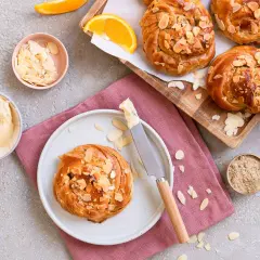 Goldbraune Kardamom-Knoten, bestreut mit Mandelblättchen, warten auf Butter und Orangenscheiben.