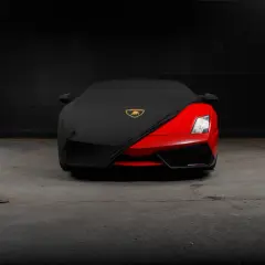 Czerwony supersamochód Lamborghini, być może najdroższe auto na świecie, częściowo przykryty czarnym pokrowcem z logo marki.