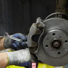 Mechanik w rękawicach dokręca śrubę przy budowie klocka hamulcowego.