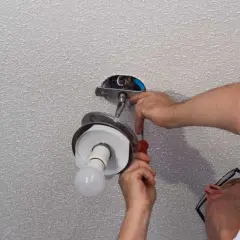 Un homme effectue le branchement d'une lampe au plafond, utilisant un tournevis pour fixer le luminaire.