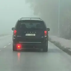 Ciemny van Dodge jedzie we mgle, włączone światła przeciwmgielne tylne poprawiają widoczność.