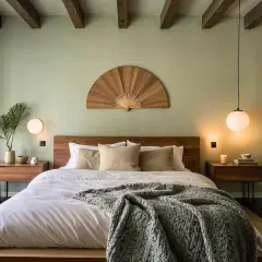 A cozy, dark bedroom with a large bed, wooden beams, and a decorative fan above the headboard.