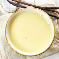 Un bol de crème anglaise onctueuse, prêt à être dégusté, avec des gousses de vanille à proximité.
