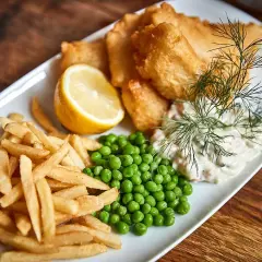 En tallrik med fish and chips, ärtor, citronklyfta och remouladsås.