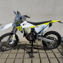 Motocykl Husqvarna WRE 125 na stojaku, biało-żółty, z logo Husqvarna.