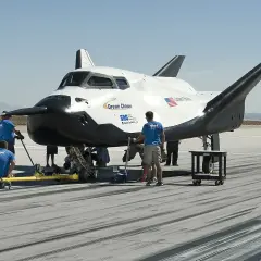Dream Chaser, kosmiczny pojazd, przygotowywany do startu. Zespół techników pracuje przy jego podwoziu na pustynnym lotnisku.