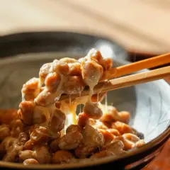Natto chinasi: attenzione alle controindicazioni. Un primo piano di natto appiccicoso sollevato da bacchette.