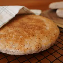 Pan de arroz redondo y dorado, cubierto parcialmente con un paño a cuadros, sobre una rejilla.