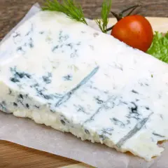 Un pezzo di gorgonzola formaggio con venature blu, guarnito con pomodorino e lattuga su tagliere di legno.