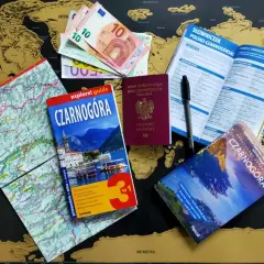 Pasport, pieniądze i przewodniki po Czarnogórze leżą na mapie świata. Czy do Czarnogóry potrzebny jest paszport? Tak, polski paszport jest widoczny.