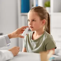 Niña recibe spray nasal para aliviar síntomas de rinitis alérgica. El doctor investiga las causas.