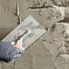 Hand mit Handschuh glättet Mörtel auf einer Wand, um einen Wanddurchbruch abzudichten.