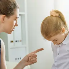 Matka karci córkę za złe zachowanie, wskazując palcem. Dziewczynka spuszcza wzrok, zawstydzona.