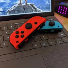 Czerwony i niebieski Joy-Con na klawiaturze laptopa, gotowe do gry. Dowiedz się, jak podłączyć Nintendo do komputera.