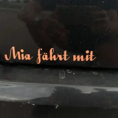 Pomarańczowa naklejka na czarnym lakierze samochodu z napisem "Mia fährt mit". Chcesz wiedzieć, jak usunąć naklejki z samochodu?