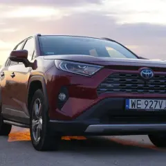 Czerwona Toyota RAV4 2.5 Hybrid na tle zachodzącego słońca nad morzem. Niskie spalanie to jej atut.