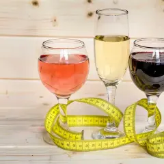 Trzy kieliszki z winem (różowym, białym, czerwonym) i miarka krawiecka. Zastanawiasz się, ile kcal ma pół litra wódki?