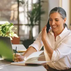 Uśmiechnięta kobieta rozmawia przez telefon, notując w zeszycie. Jej **list intencyjny** jest gotowy do wysłania.