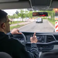 Kierowca w okularach wskazuje palcem na ekran nawigacji, gdy zbliża się do drogi dla pieszych.