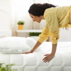 Kobieta sprawdza, jaka kołdra na łóżko 160x200 będzie najlepsza. Biała, pikowana kołdra i poduszka leżą na łóżku.
