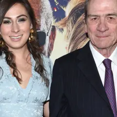 Tommy Lee Jones z żoną, uśmiechnięci na tle plakatu filmowego.