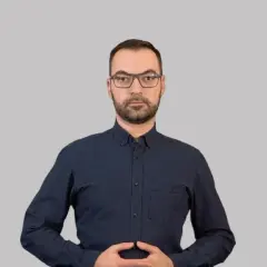 Mężczyzna w okularach i granatowej koszuli, z dłońmi złożonymi na brzuchu. Widoczne logo Euronet i Migam. Proces euronet rejestracja id.