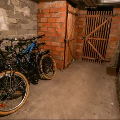 Wspólna piwnica w bloku, gdzie stoją rowery. W tle drewniane drzwi i ceglane ściany.