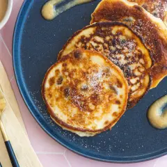 Goldene quarkkeulchen ohne kartoffeln, bestreut mit Zucker, serviert mit Apfelmus auf einem dunklen Teller.