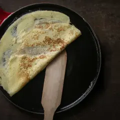 Ein goldbrauner Crêpe wird in einer Pfanne mit einem Holzspatel gefaltet. Perfekt für ein einfaches Crêpe Rezept.