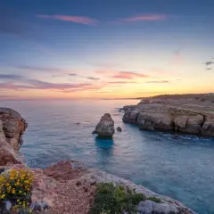 Sonnenuntergang an Menorcas Küste. Felsen, türkises Wasser und ein pastellfarbener Himmel – perfekte Menorca Urlaub Tipps für Romantiker.