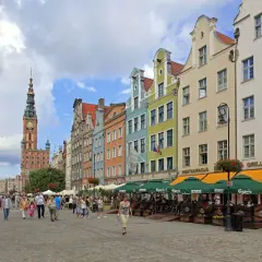 Färgglada hus längs en livlig gågata på långa marknaden Gdansk. Folk promenerar och njuter av solen vid uteserveringar.