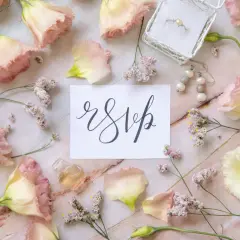 Delikatne kwiaty, pierścionek i kolczyki otaczają kartkę z napisem "rsvp". Czy wiesz, rsvp co to znaczy?