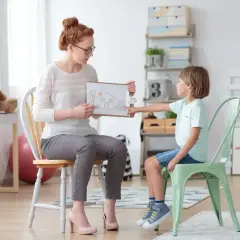 Terapeuta pokazuje rysunek domu dziecku, które może potrzebować wsparcia związanego z niepełnosprawnością intelektualną w stopniu lekkim, być może w kontekście zasiłku.