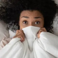 Ojos asustados de mujer con cabello rizado, escondida bajo la sábana, como si soñar que te apuñalan.