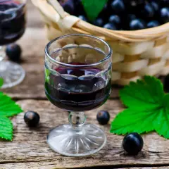 Aksamitna nalewka z czarnej porzeczki w kieliszku, obok koszyk pełen owoców i liści.