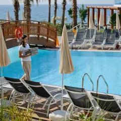 Pracownica hotelu niesie ręczniki przy basenie w Avsallar. W tle widać morze i palmy.